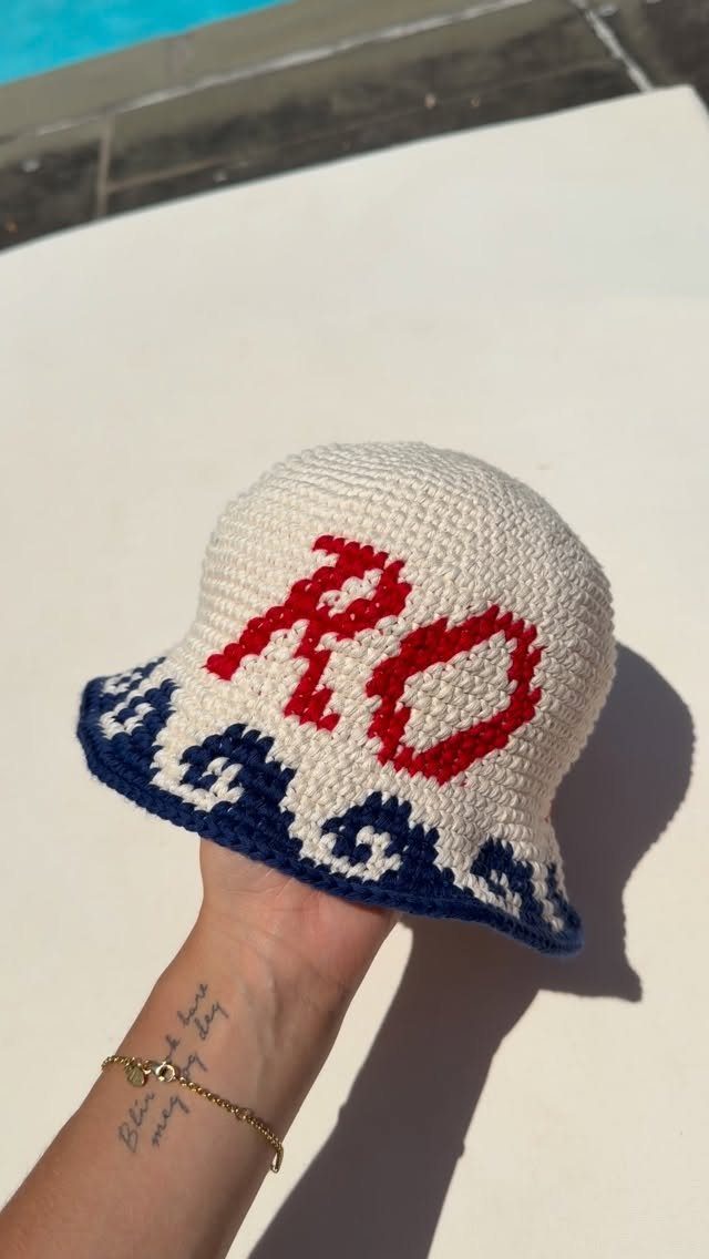 Crocheted white bucket hat with red letters RO and blue wave patterns.