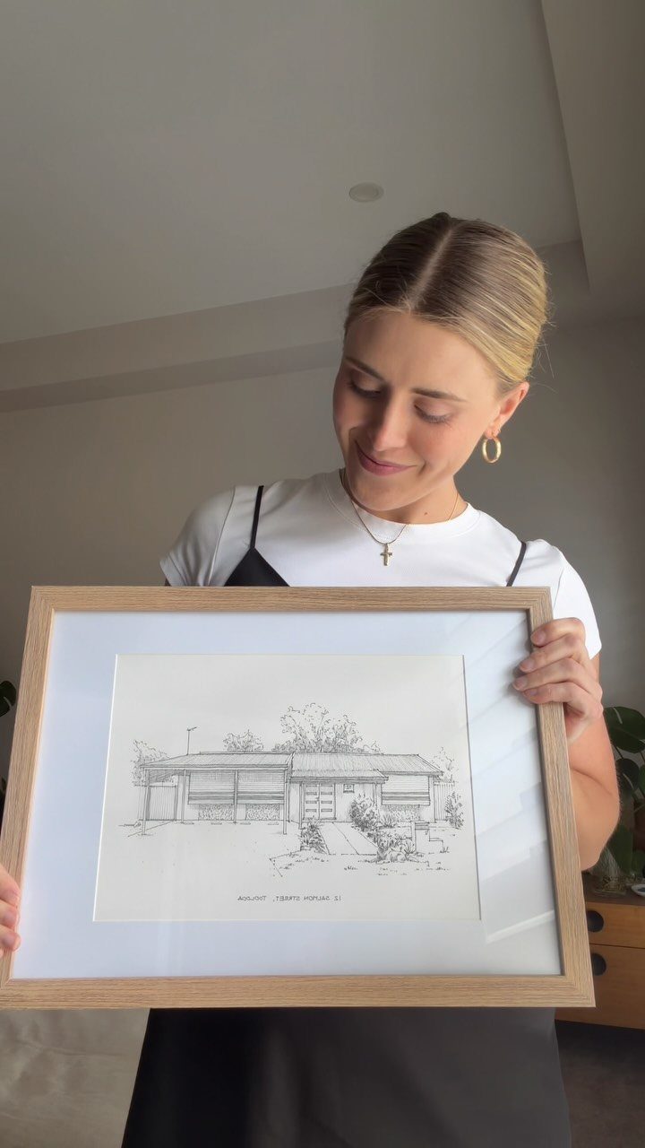 Woman holding a framed black and white architectural sketch of a residential home.