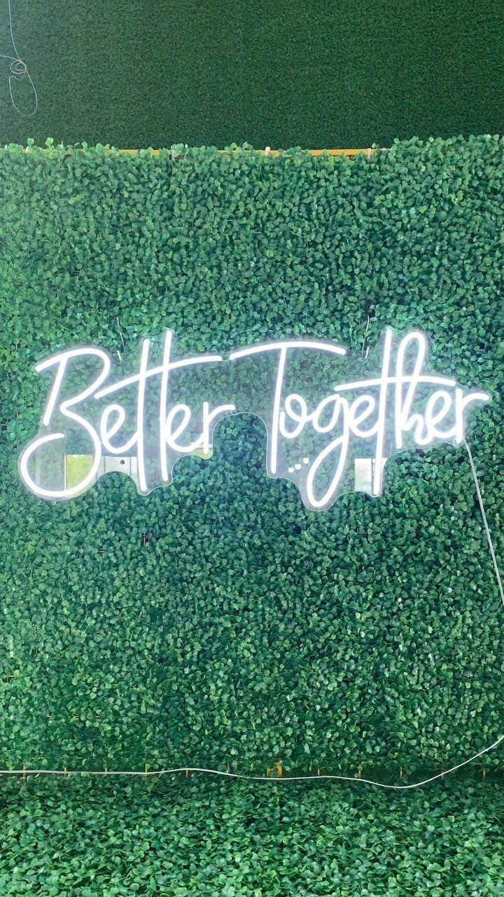 White neon sign saying Better Together mounted on a green leaf wall