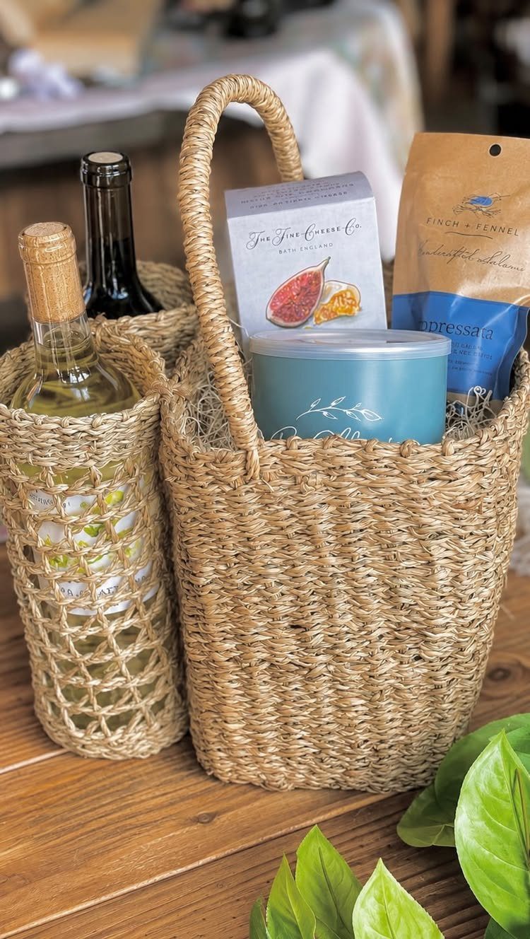 Woven straw gift basket with candle and snacks next to bottled wine.