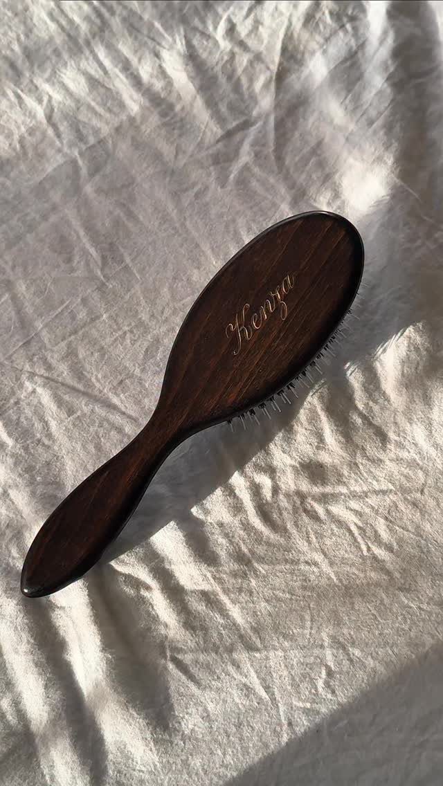 Wooden hairbrush with gold engraved name resting on white wrinkled fabric.