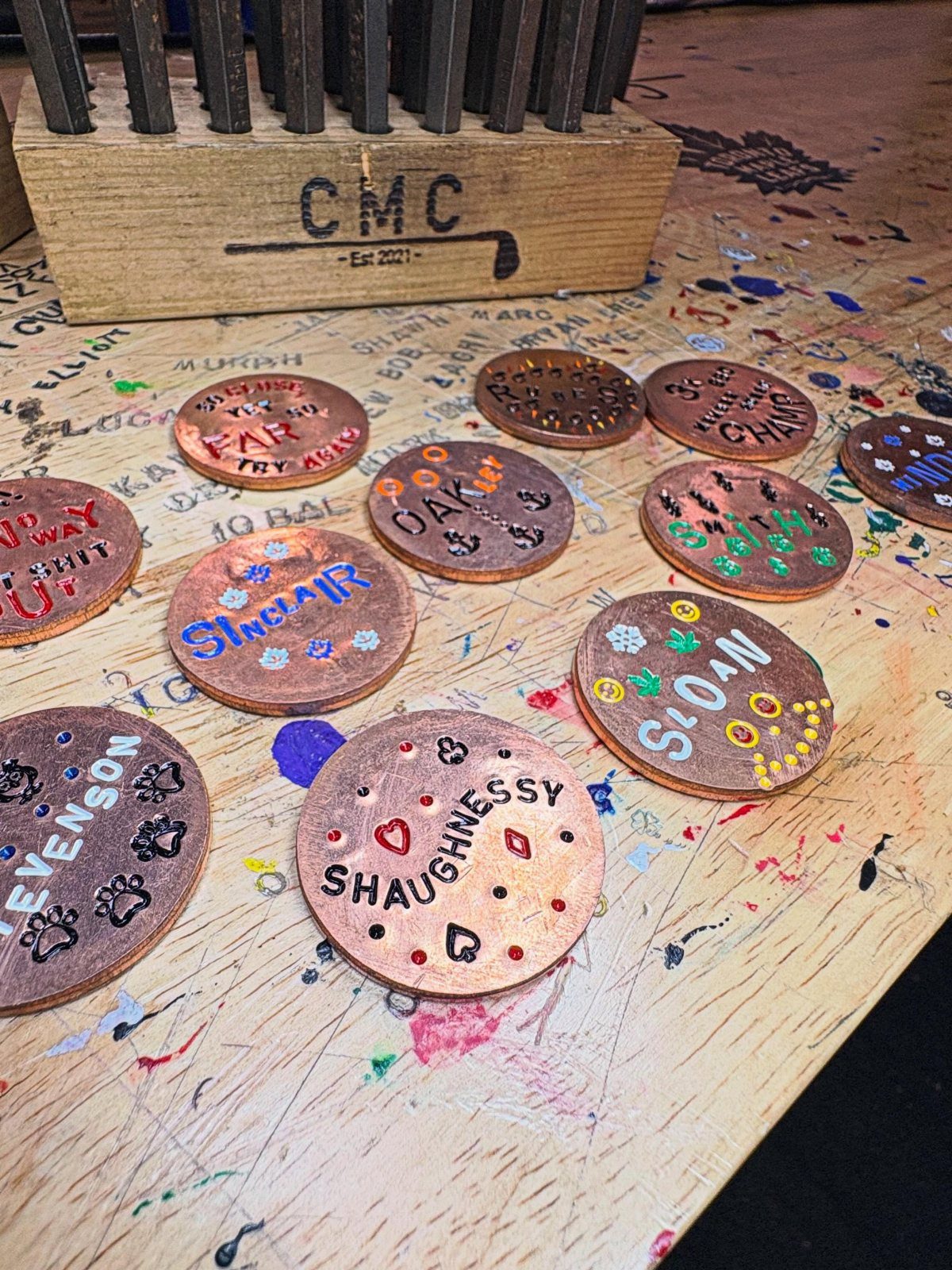 Hand-painted personalized copper discs with names and colorful art on a wooden workbench