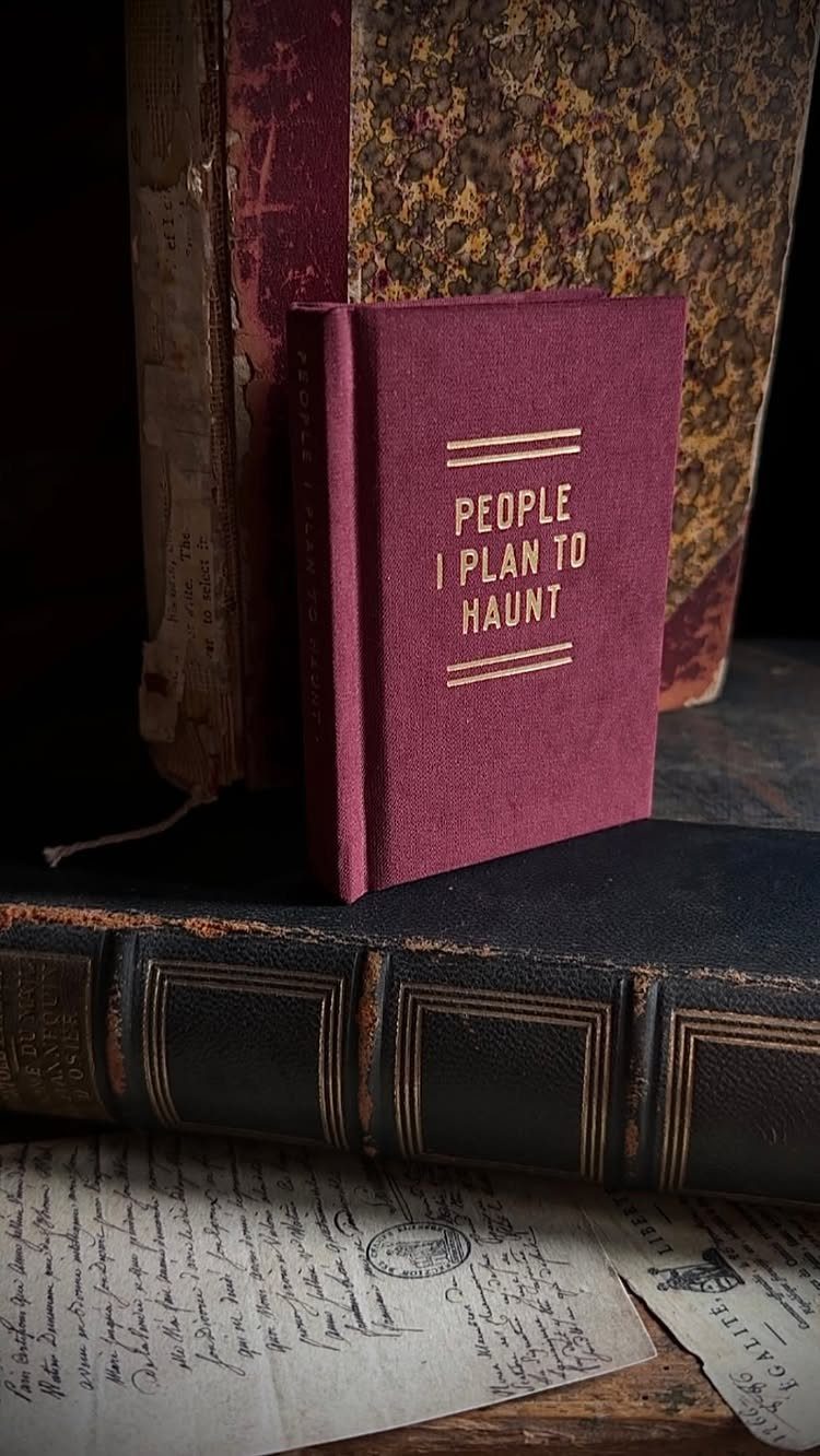 Burgundy notebook titled People I Plan To Haunt among antique leather books