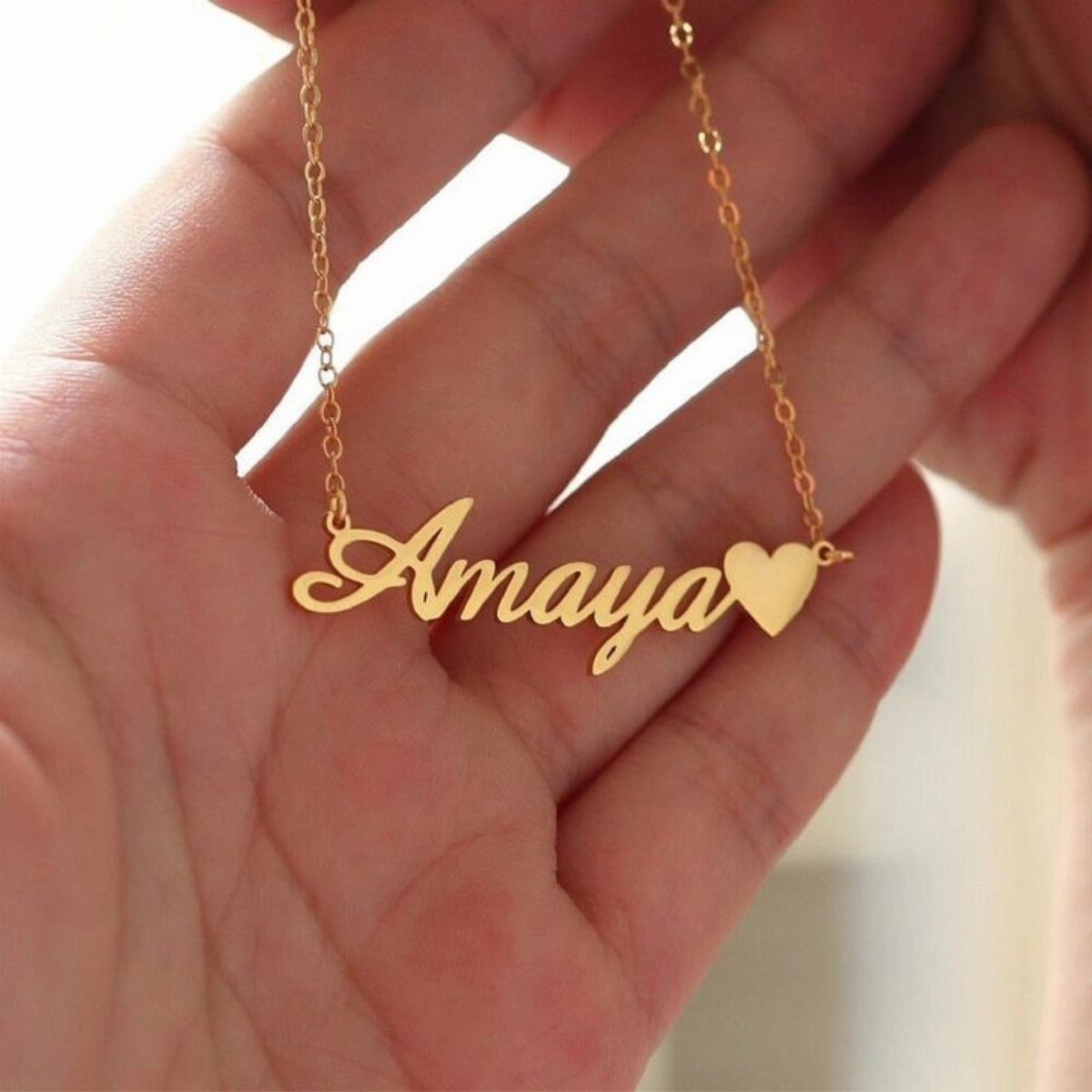 Gold name pendant necklace reading Amaya with a heart held in a hand
