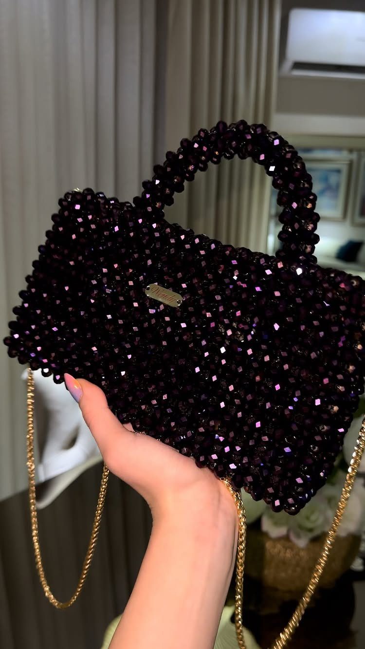 Dark purple beaded handbag with a gold chain strap held by a hand.