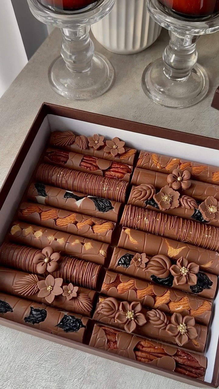 Assorted gourmet chocolate cylinders with floral decorations in a brown gift box