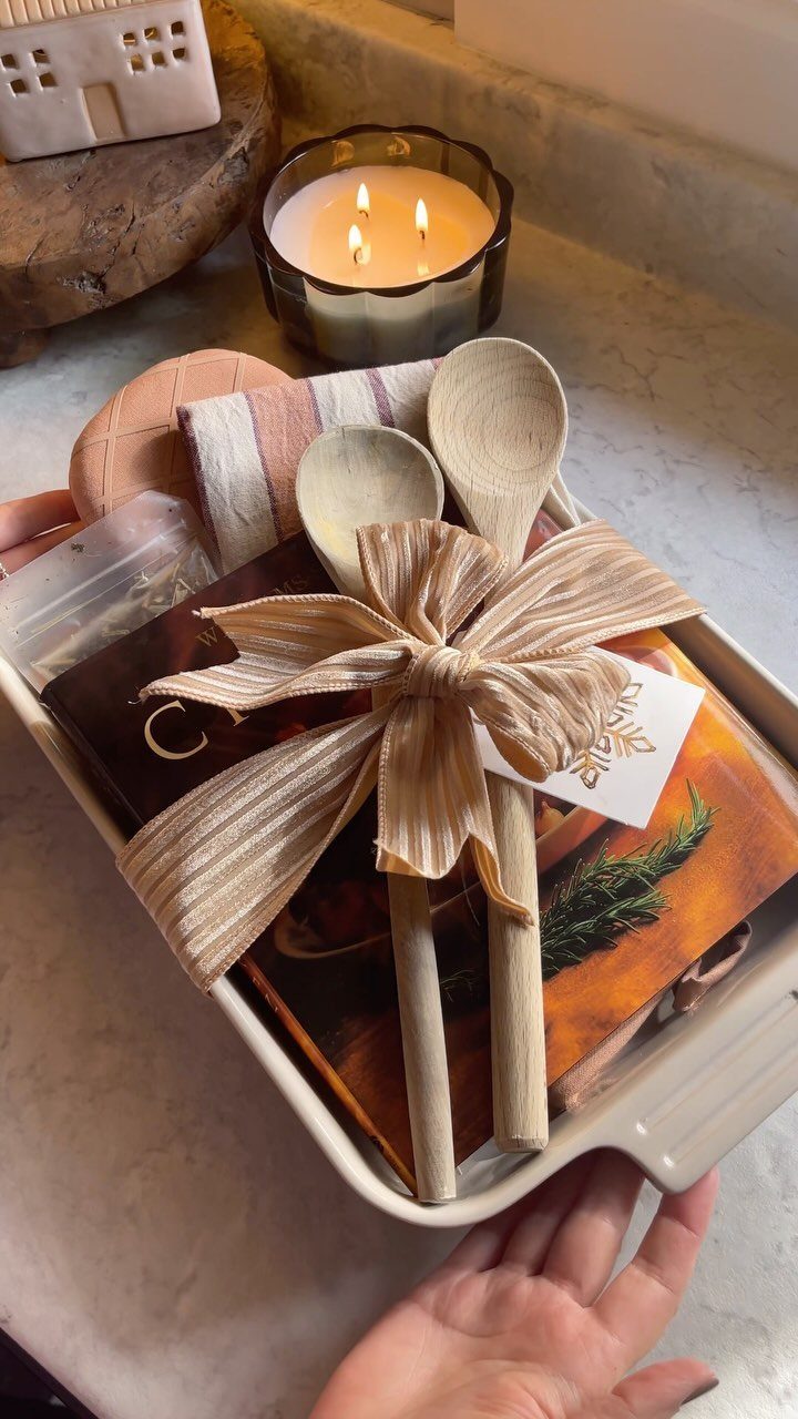 Gift tray with wooden spoons, a cookbook, a candle, and a kitchen towel.