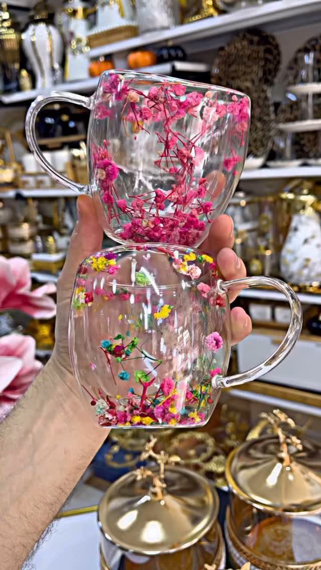 Two clear glass mugs filled with colorful preserved dried flowers held by a hand.