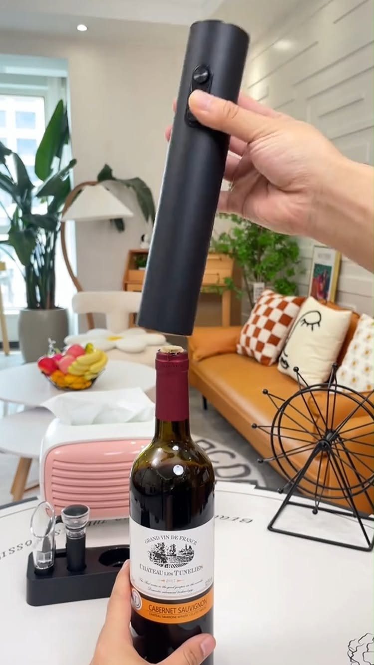 Black electric cordless wine opener being used to open a red wine bottle.