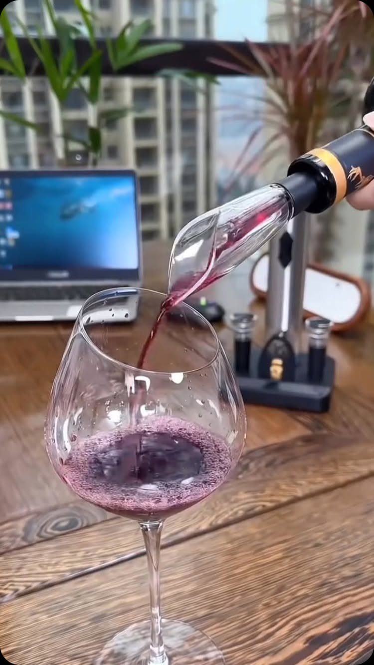 Red wine pouring from an electric aerator into a glass on wooden table