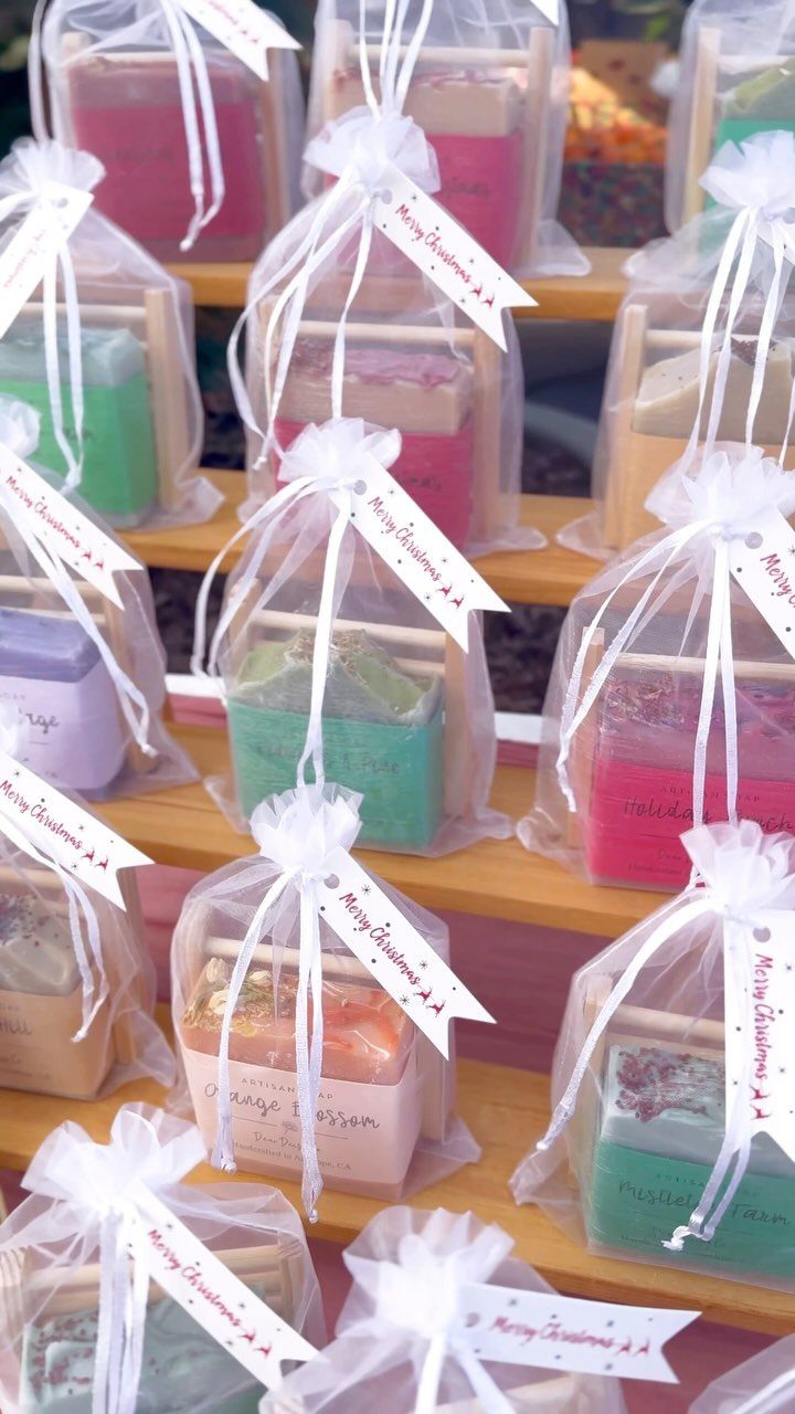 Handmade colorful soap bars in clear gift bags with Christmas tags on wooden shelves.