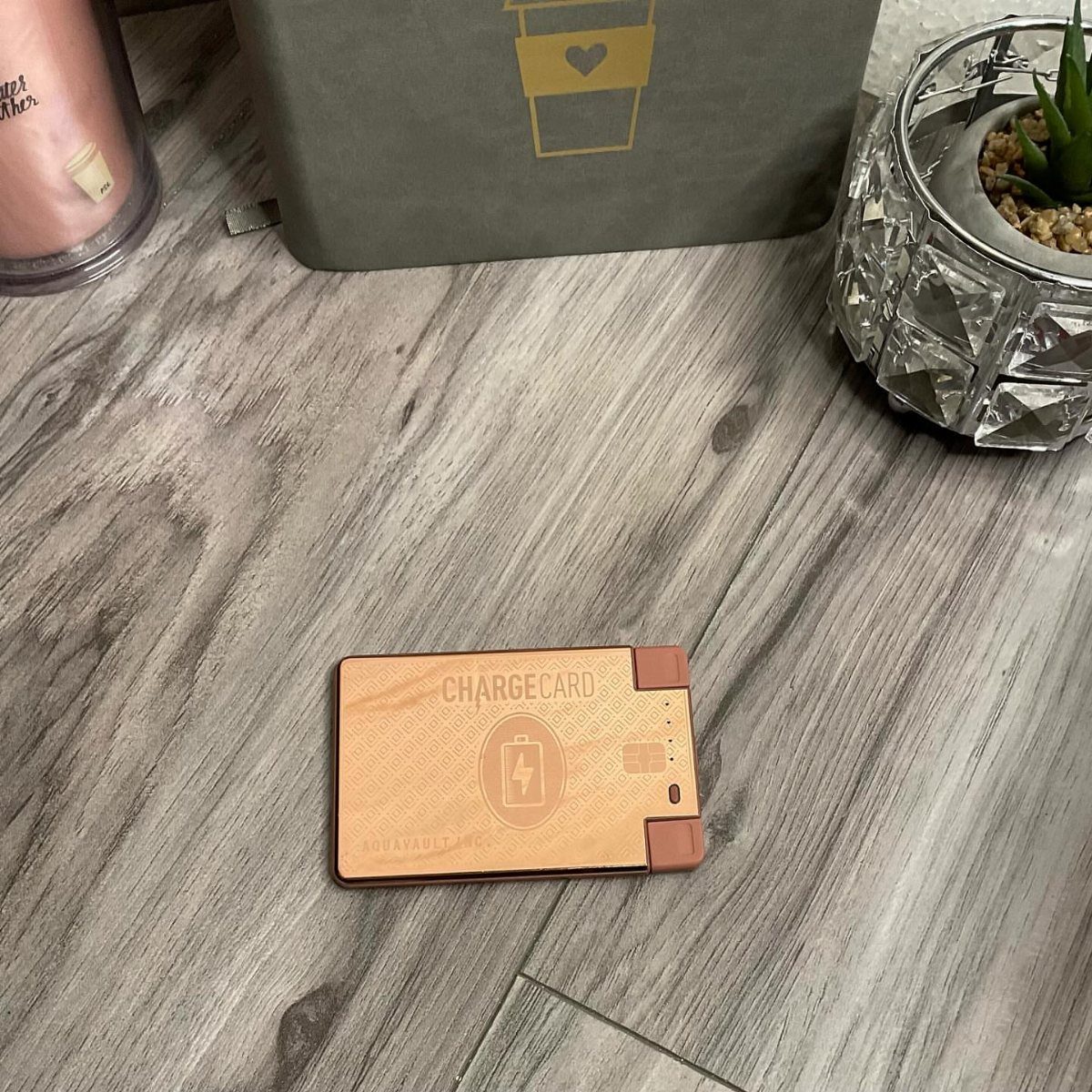 Wood-grain portable power bank called ChargeCard resting on a grey wooden floor.