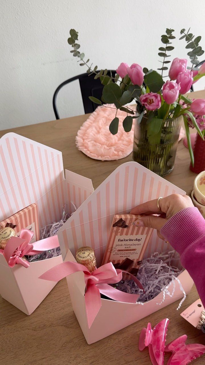 Pink striped gift boxes with treats and ribbons next to pink tulips.