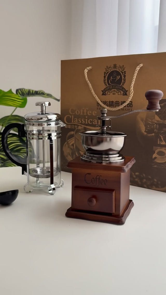 Manual wooden coffee grinder and glass French press on a white table
