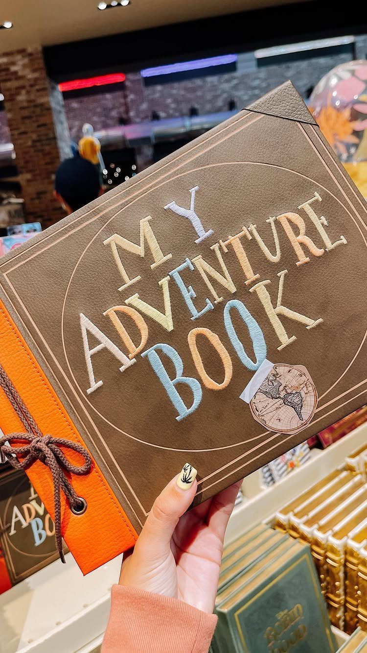 Brown fabric scrapbook with colorful embroidered text reading My Adventure Book held by hand