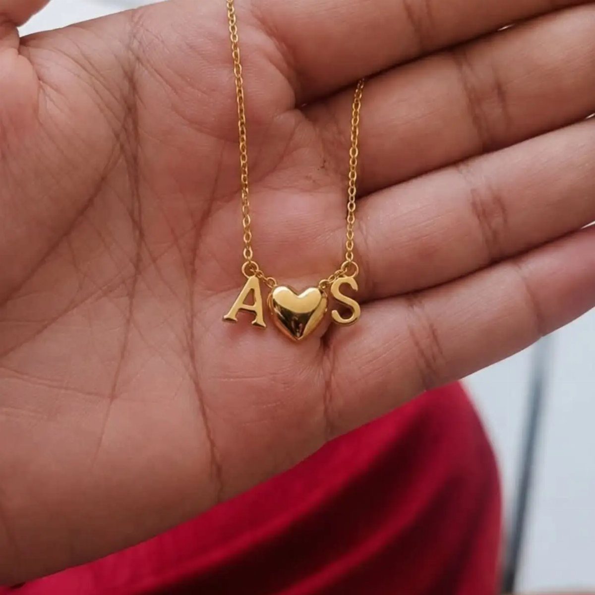 Gold necklace with heart pendant and initials A and S held in palm