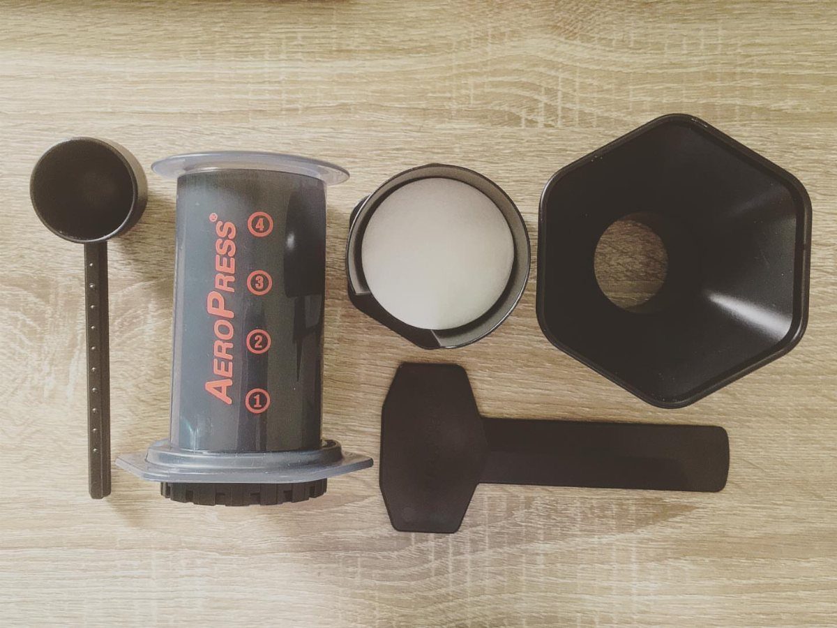 AeroPress coffee maker and accessories arranged on a light wooden tabletop.
