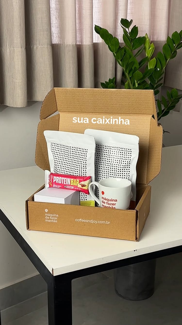 Cardboard gift box containing coffee pouches, a protein bar, and a white mug.