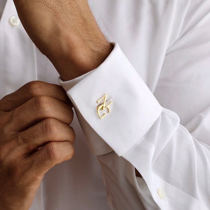 Gold monogrammed cufflink on the sleeve of a crisp white dress shirt.