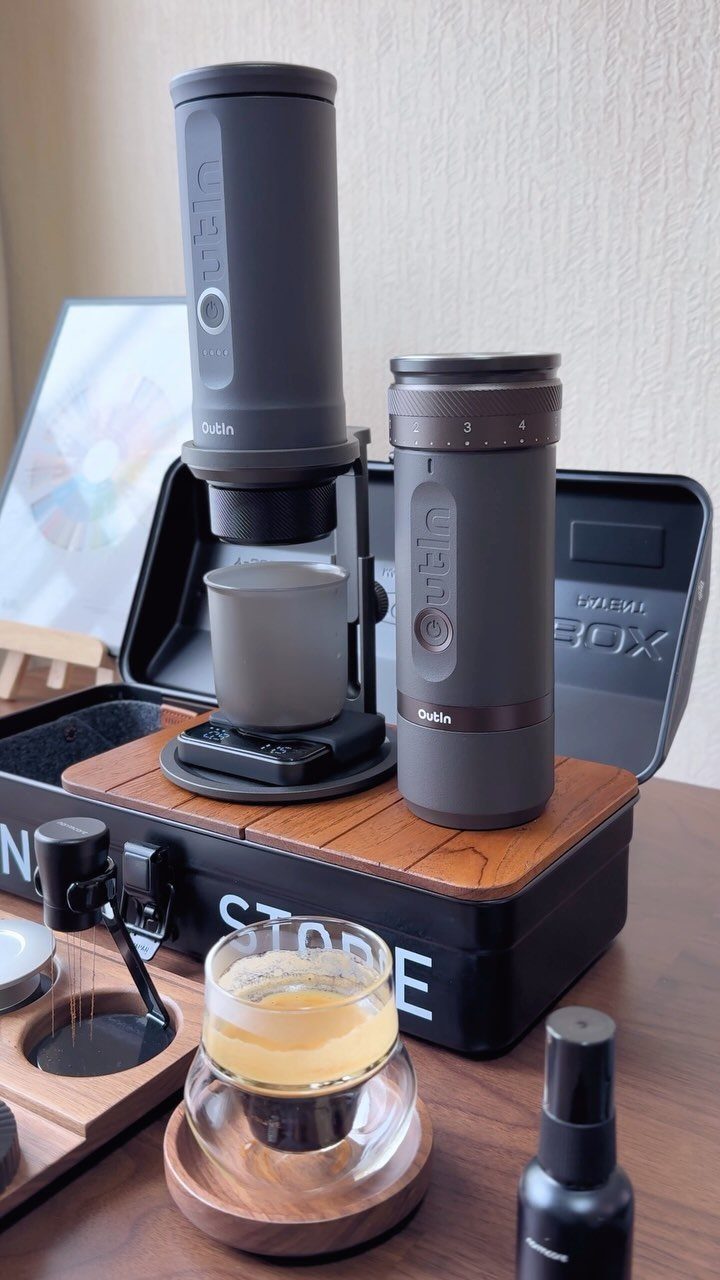Portable espresso maker and travel mug set with a small glass of coffee.