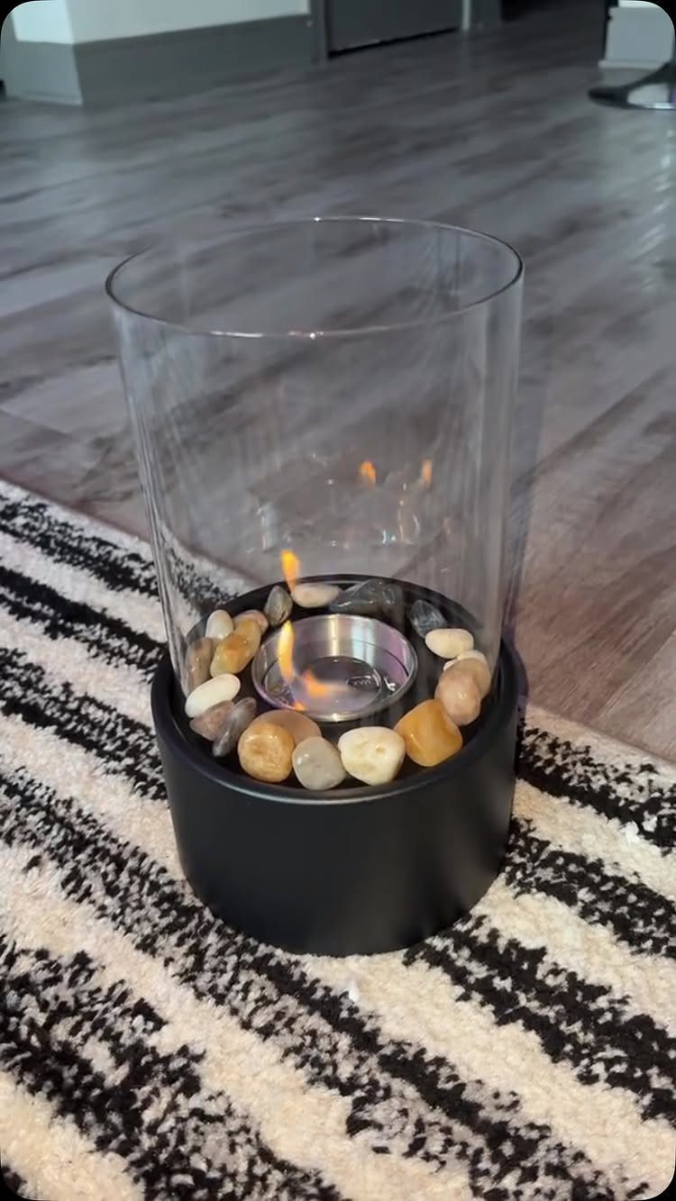 Tabletop fire pit with river stones and flame inside a glass cylinder.