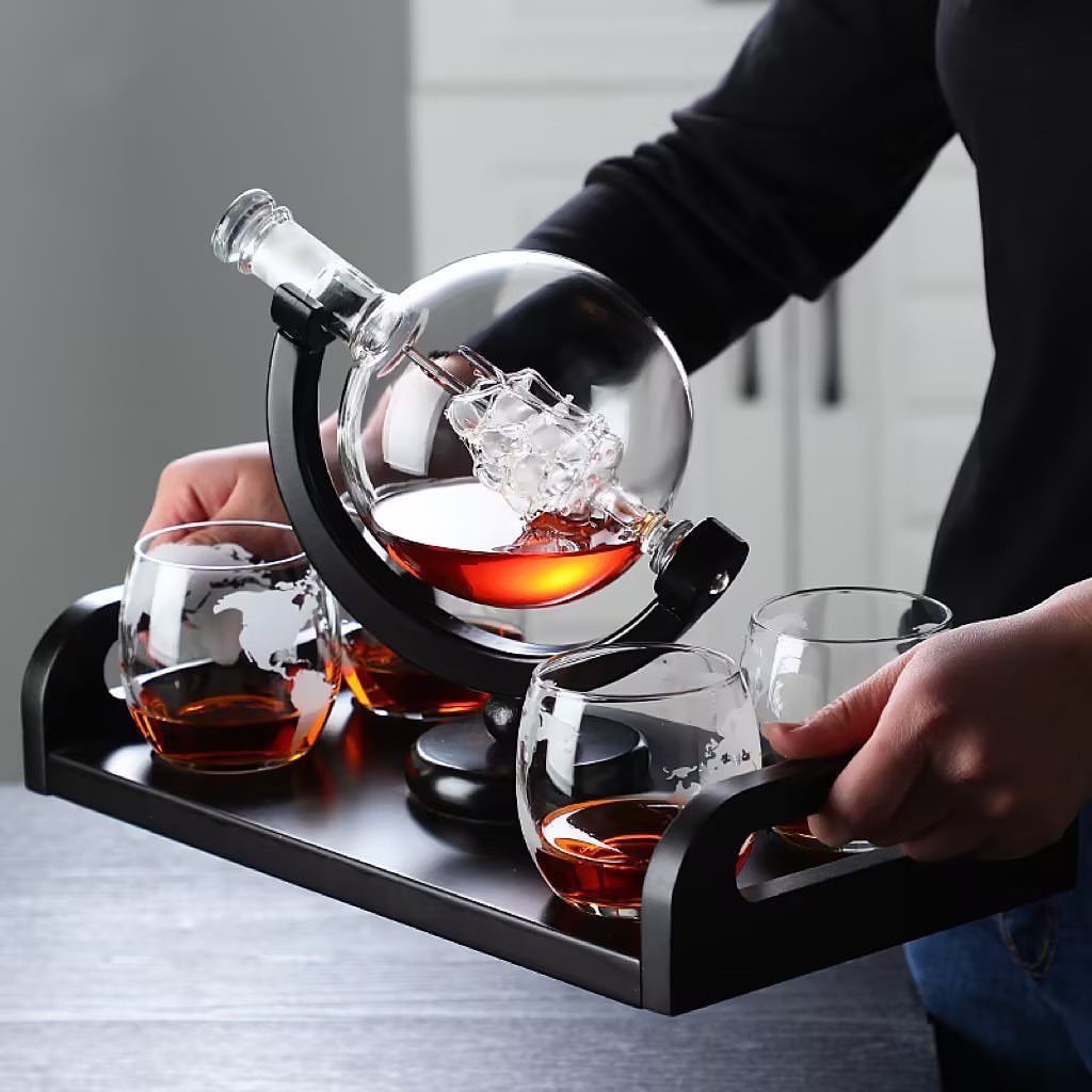 Globe-shaped whiskey decanter and glasses on a black tray held by a person.