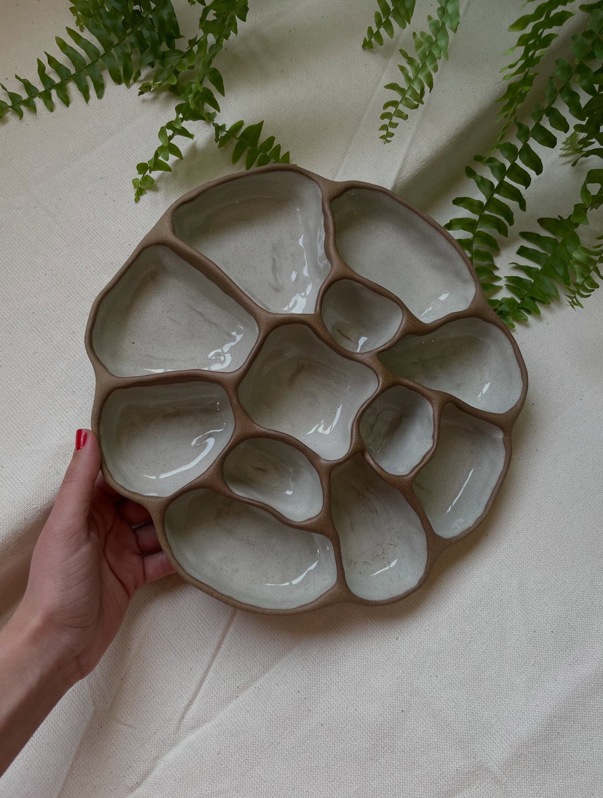 Ceramic divided tray with organic shapes held by a hand over white fabric.