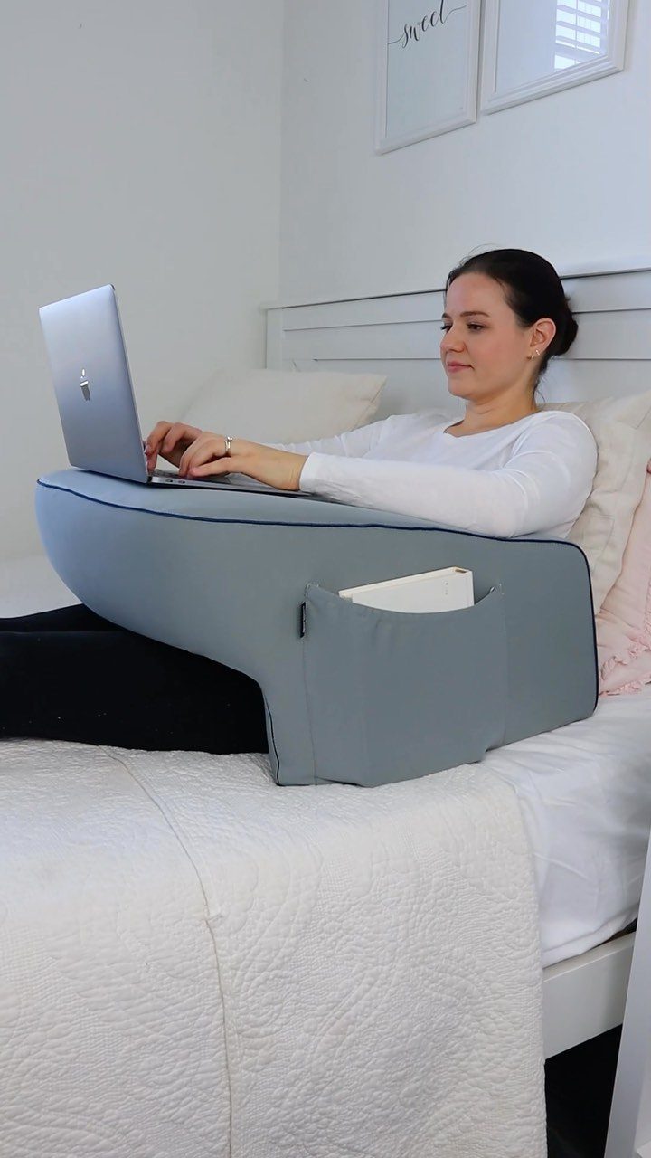Woman using a laptop on a grey fabric lap desk while sitting in bed