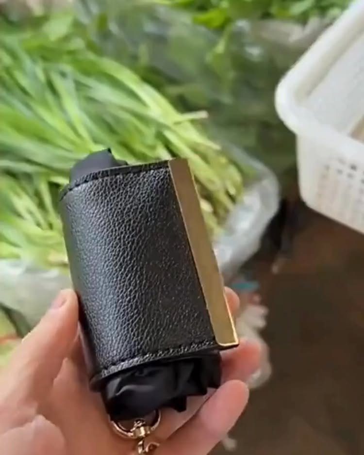 Small black leather keychain pouch with gold accent held in a hand.