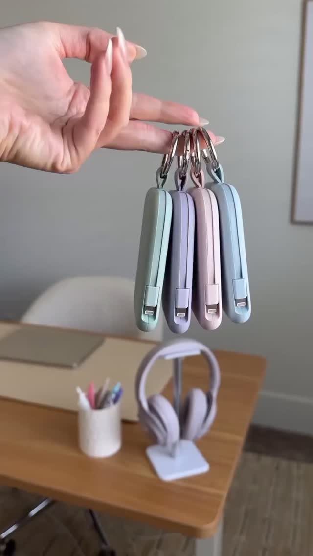 12 Useful Gifts for Men: From Chef's Knives to Multitools 5 Four pastel-colored portable charger keychains held by a hand over a desk.