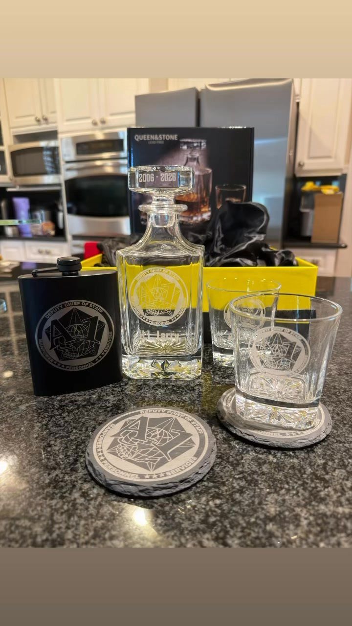 Engraved barware gift set with decanter, glasses, and flask on a granite counter.