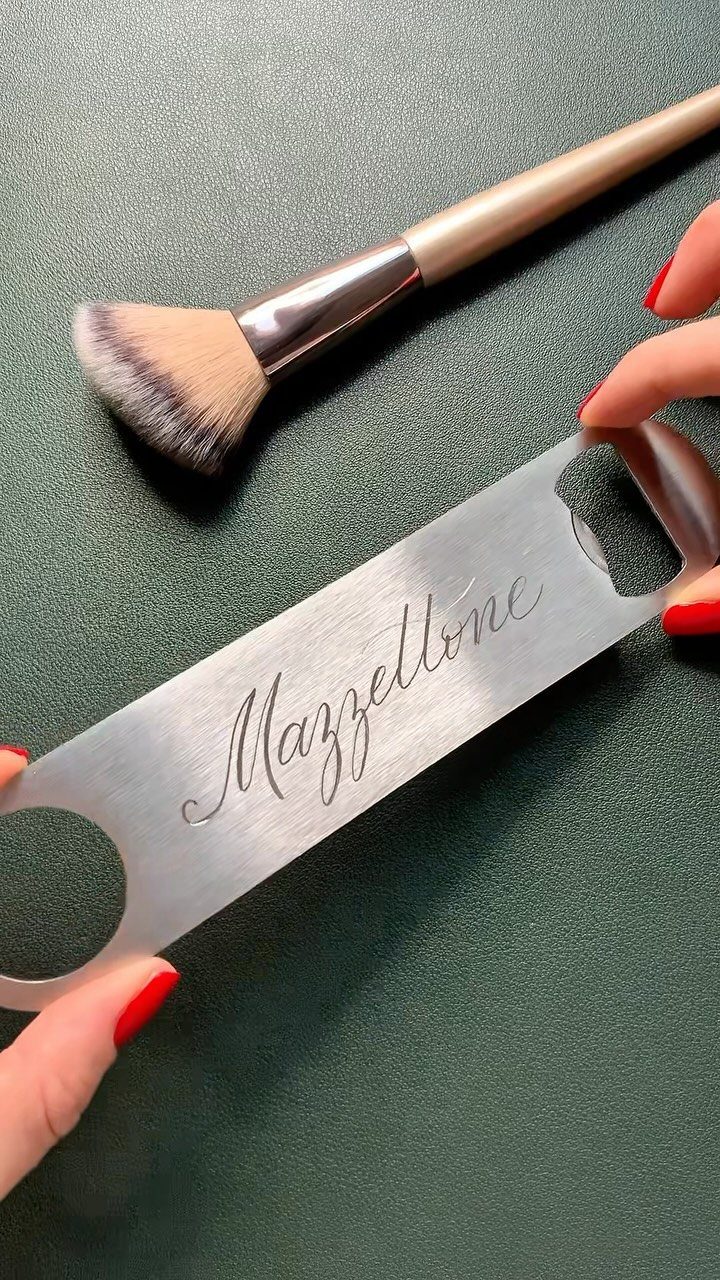 Silver engraved metal bottle opener held by hands with red nail polish