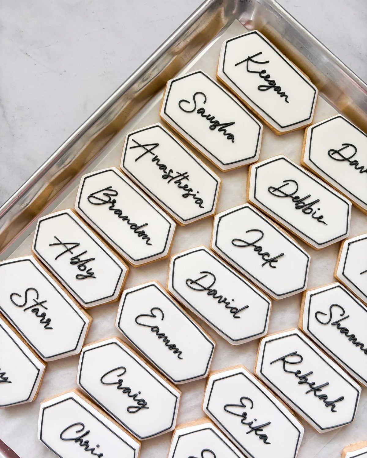 Hexagonal sugar cookies with personalized names in black icing on a metal tray.