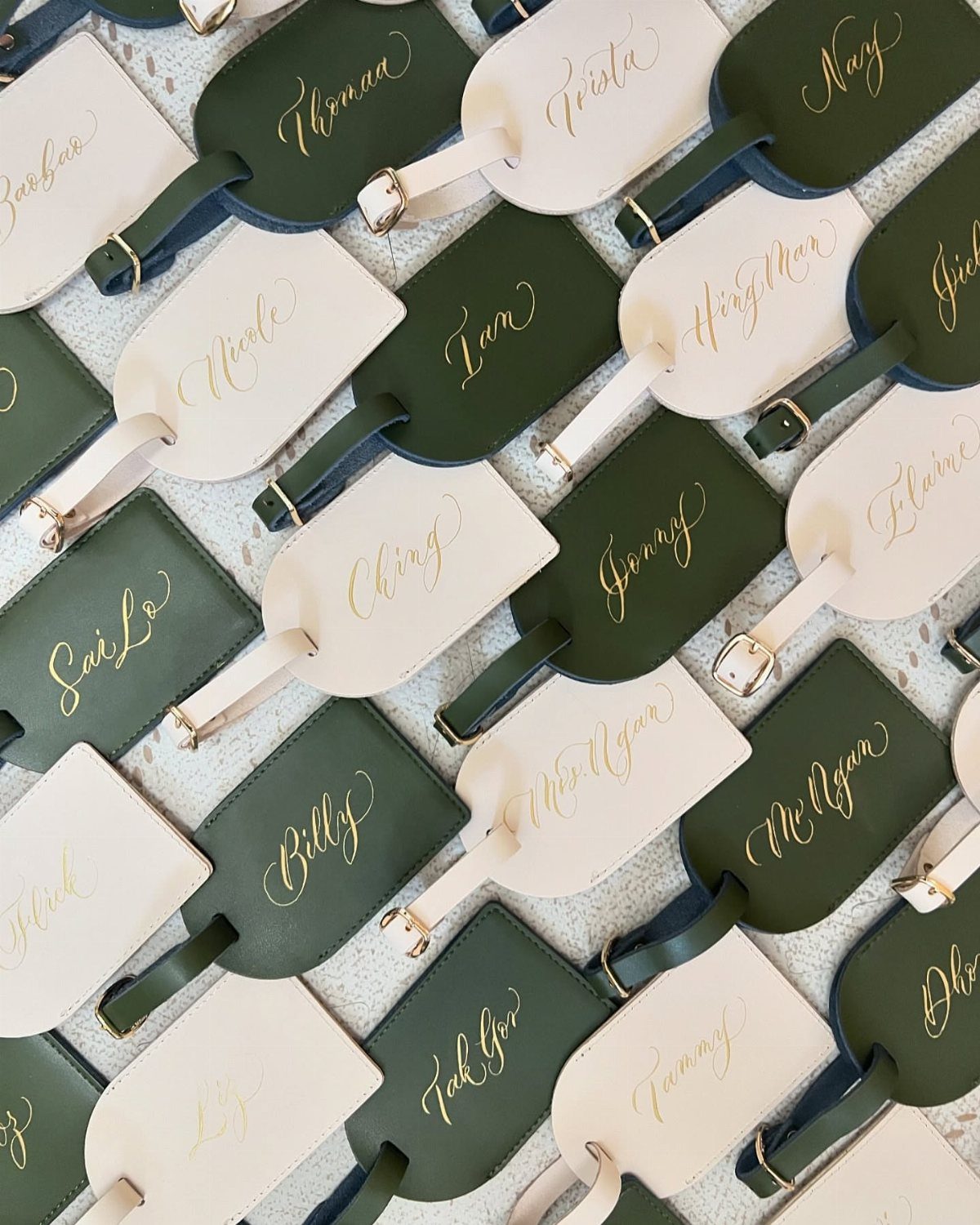 Leather luggage tags in green and cream with gold calligraphed names for wedding guests.