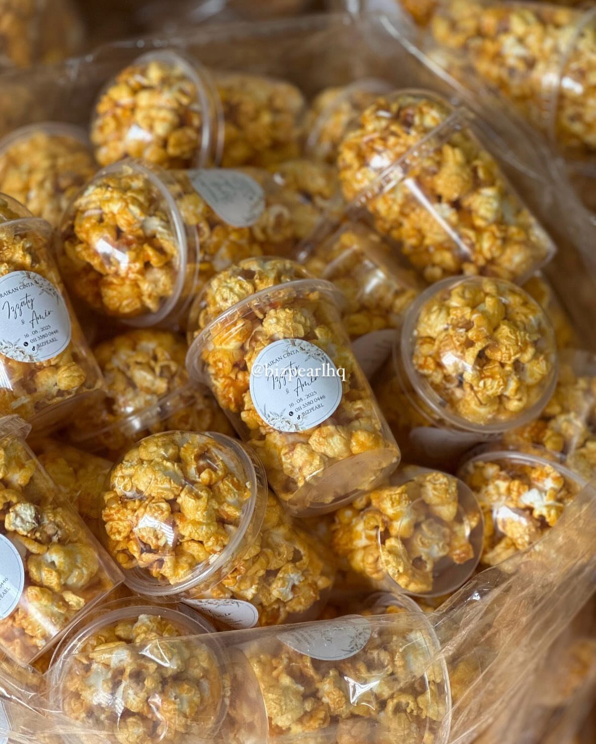 Caramel popcorn in small clear plastic cups with white labels for wedding favors.