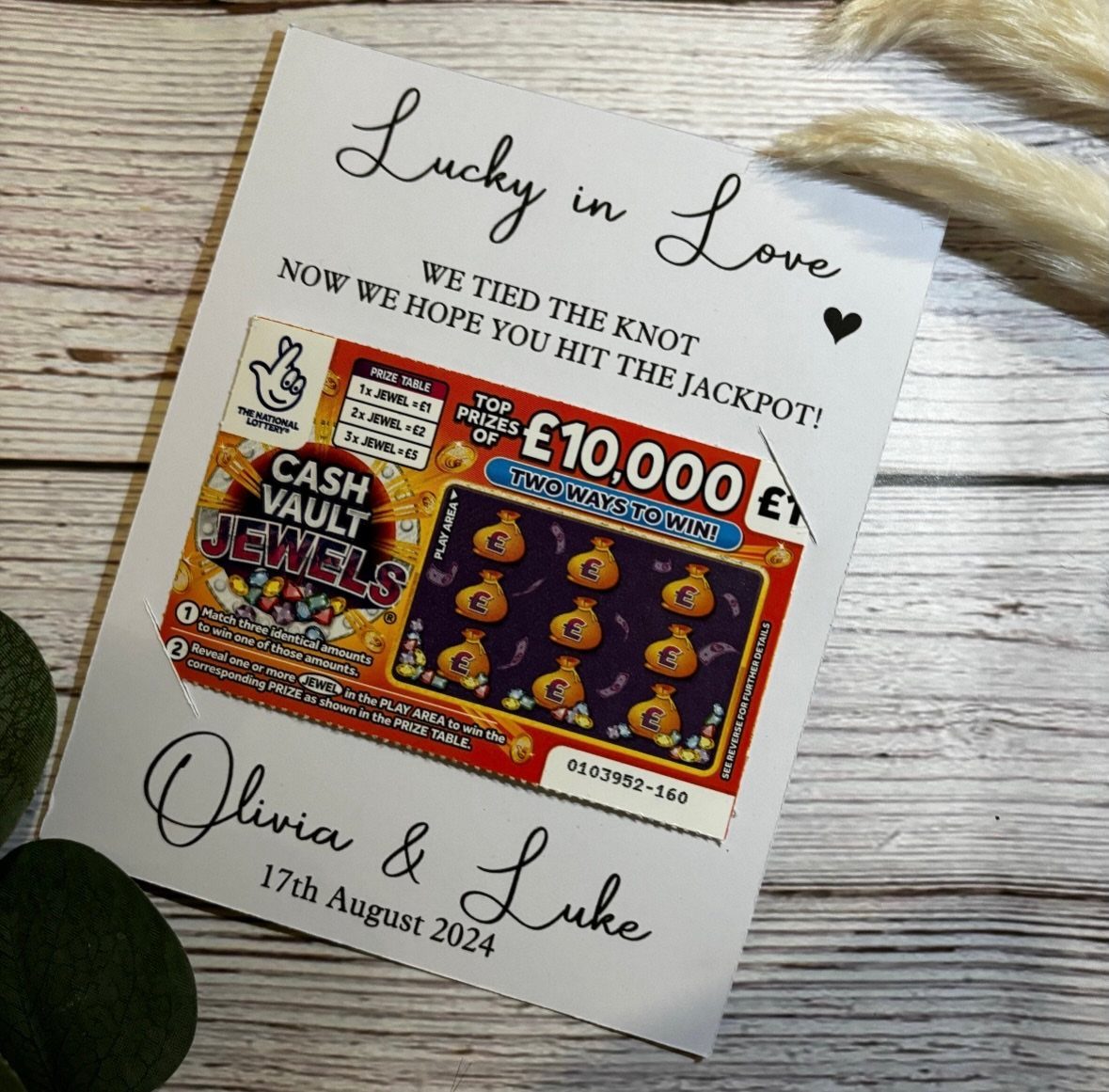 Lottery scratch card attached to a personalized white wedding favor card on wood.