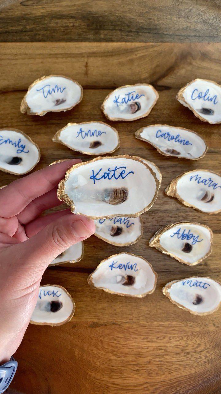 Gold-edged oyster shells with handwritten names used as place cards on wooden table