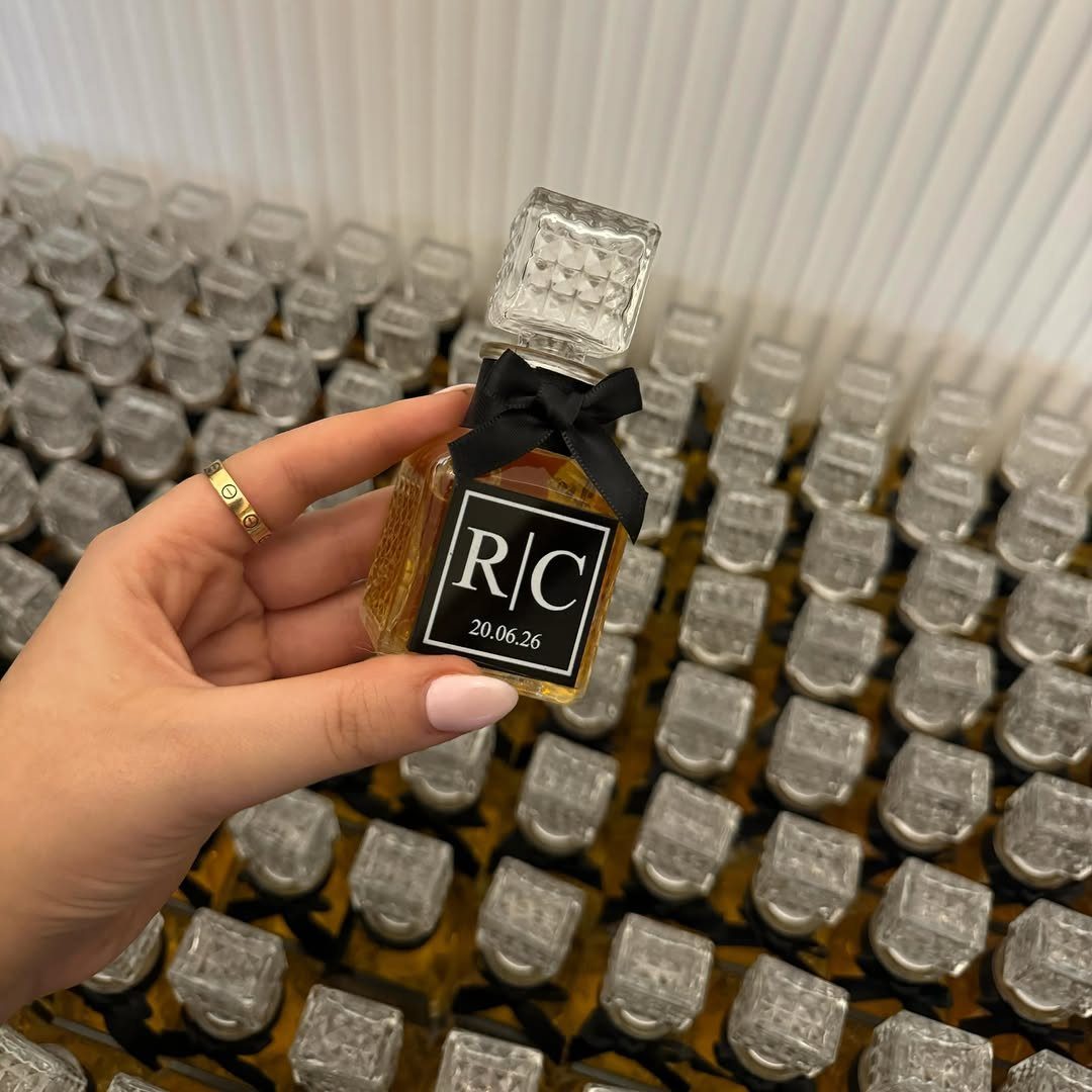 Small square glass liquor bottle with black ribbon and personalized label held by hand.