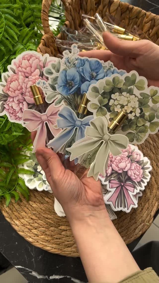 Small glass perfume vials with floral paper tags held in a person's hands.