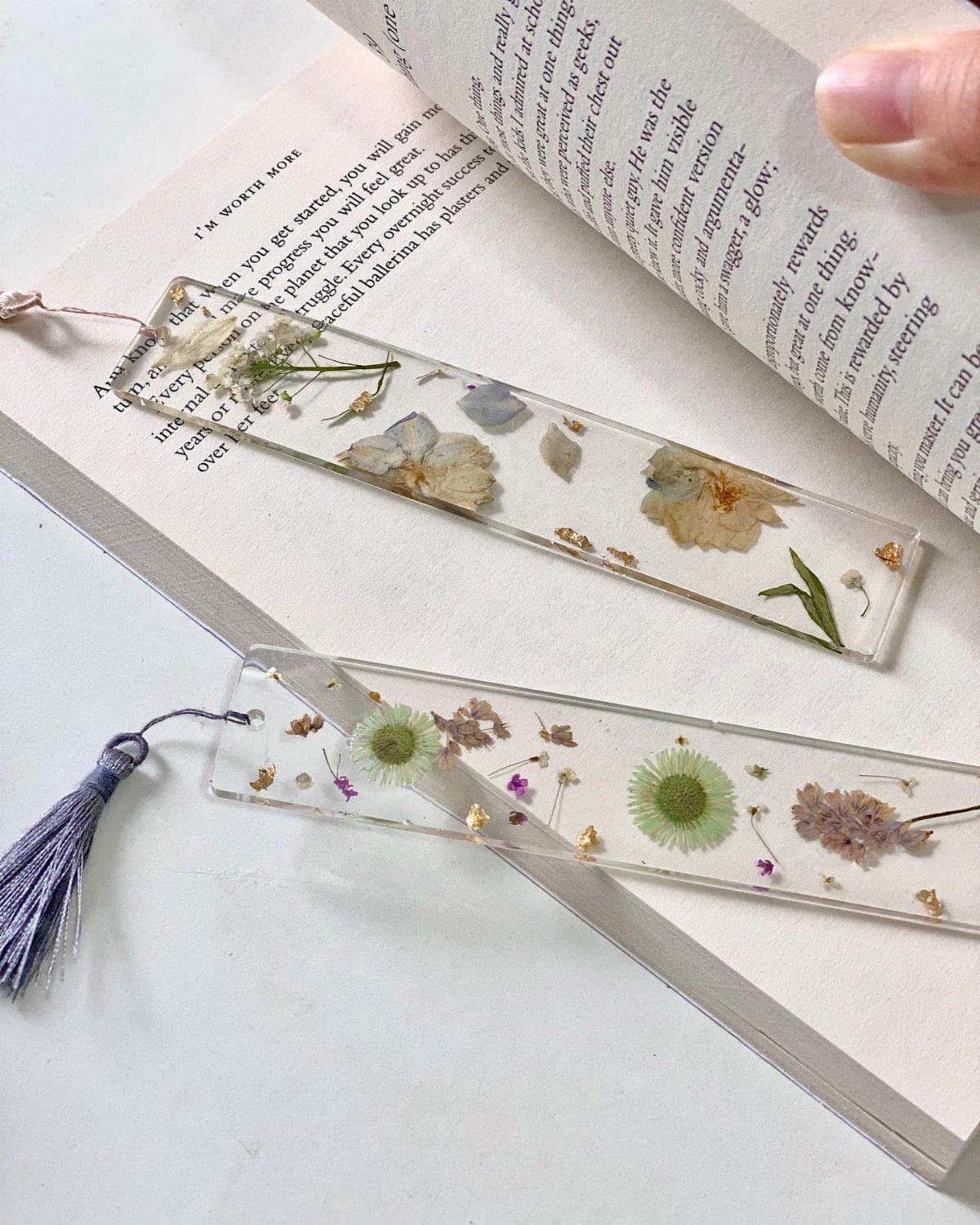 Clear acrylic bookmarks with pressed dried flowers tucked into an open book.