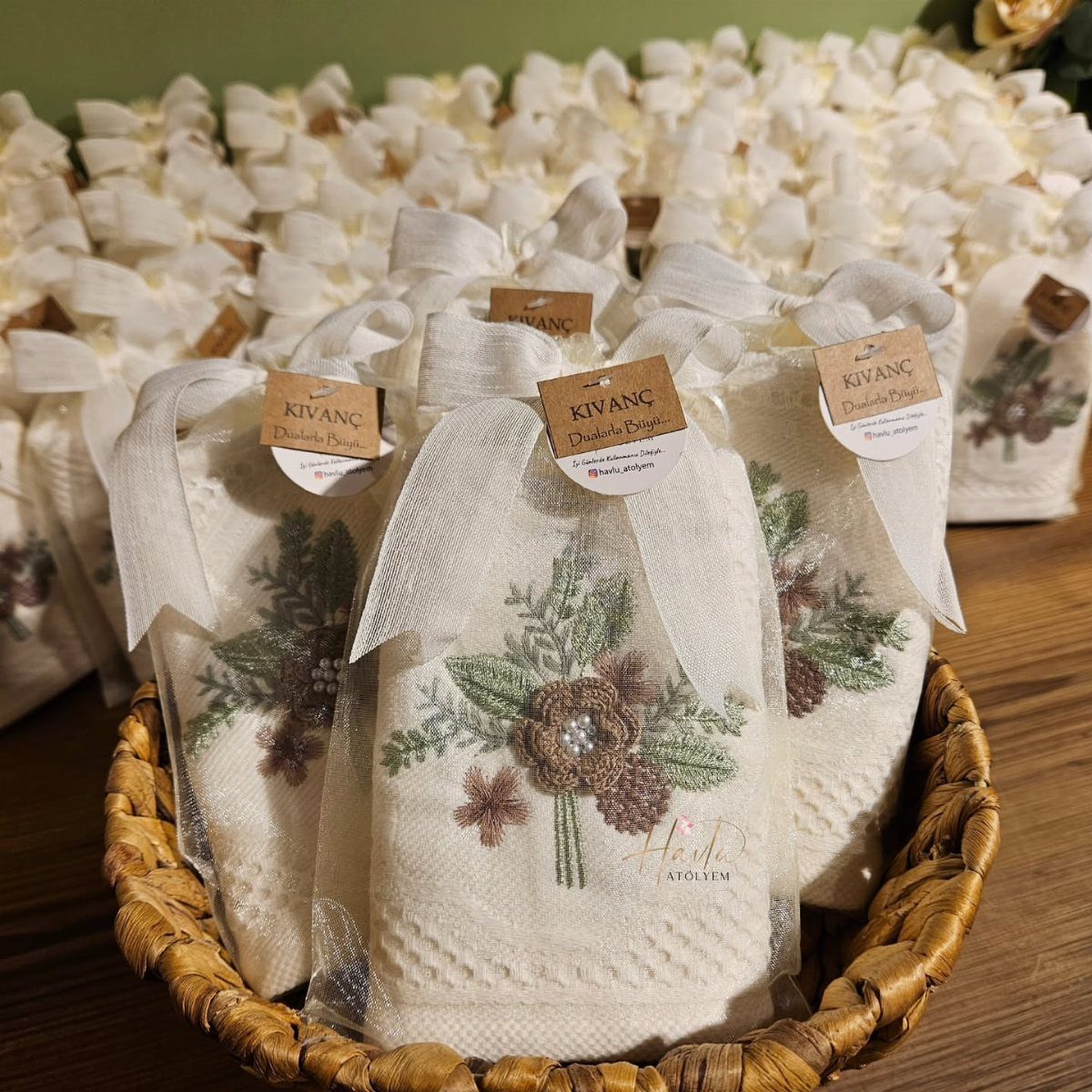 Embroidered white rolled towels tied with ribbons in a woven wicker basket