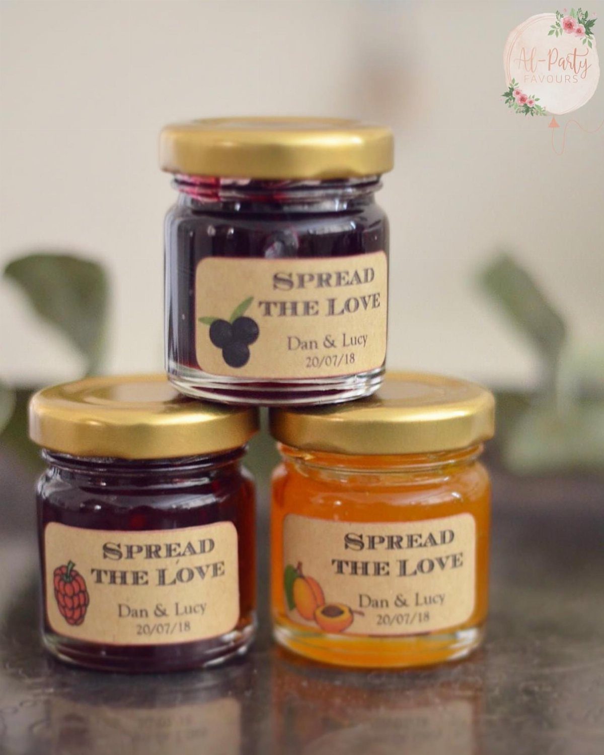 Three mini jam jars with gold lids and rustic wedding labels stacked together.