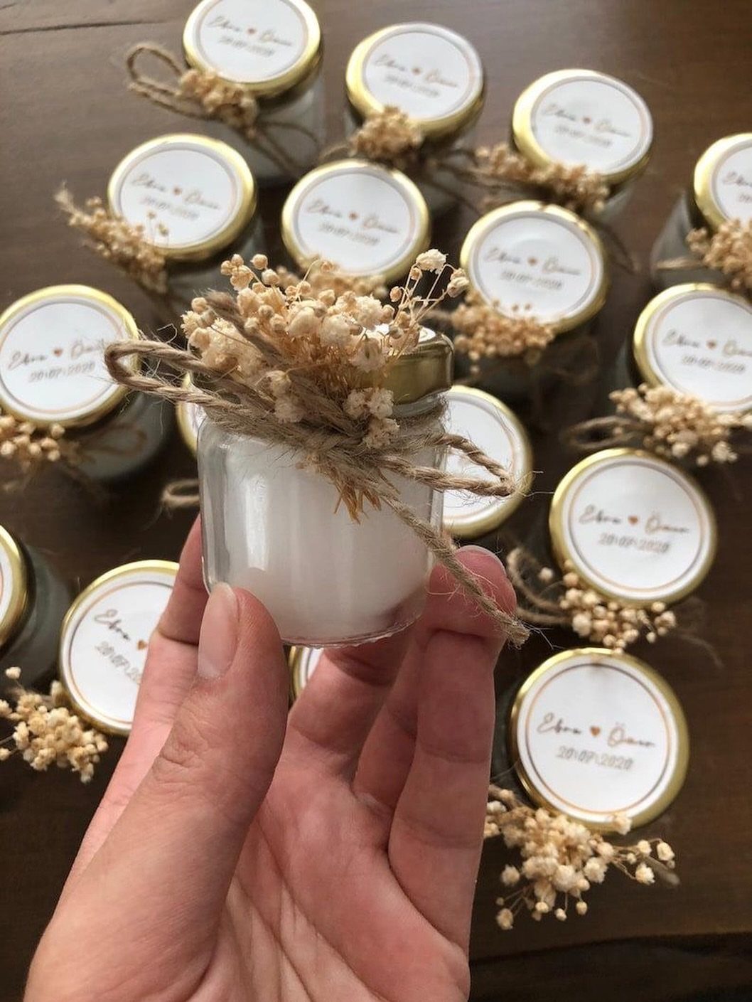 Small white scented candles in glass jars with twine and dried flowers.