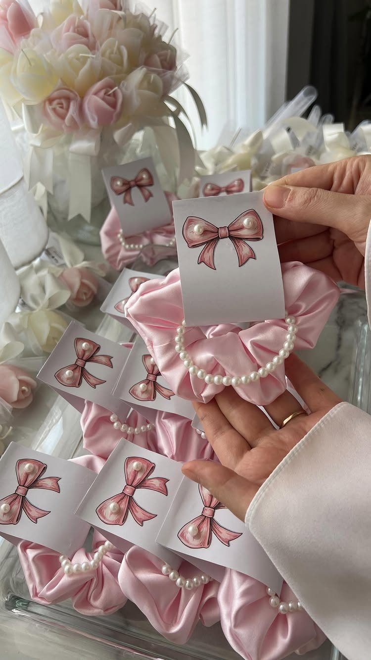 Pink satin scrunchies with pearl accents and bow cards as wedding favors.
