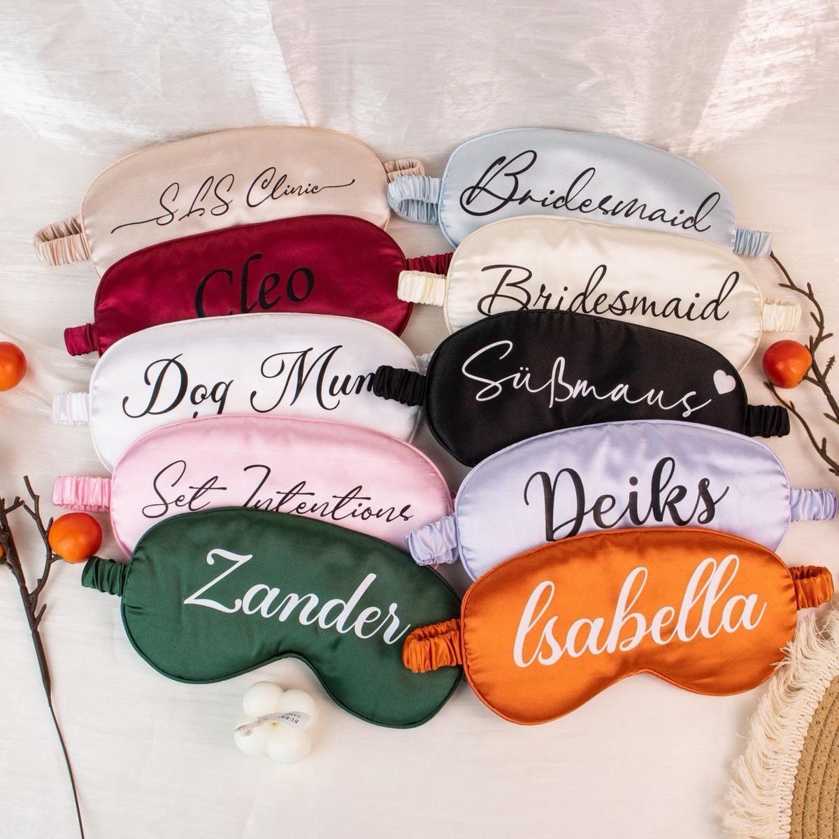 Colorful satin sleep masks with personalized names and titles arranged on white fabric.