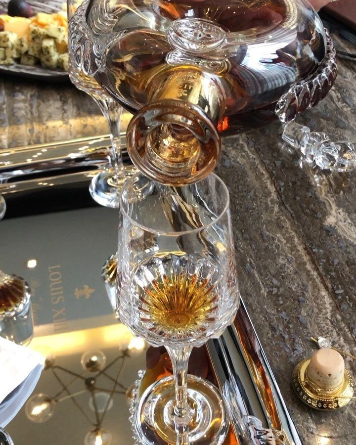 Golden liquor pouring from a crystal decanter into a matching crystal glass on silver.