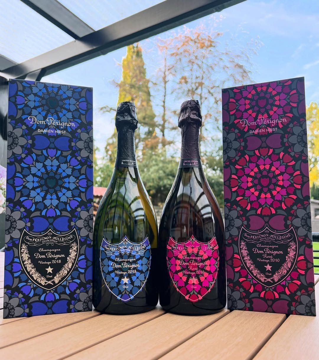 Two bottles of Dom Perignon champagne with matching patterned gift boxes on a table.
