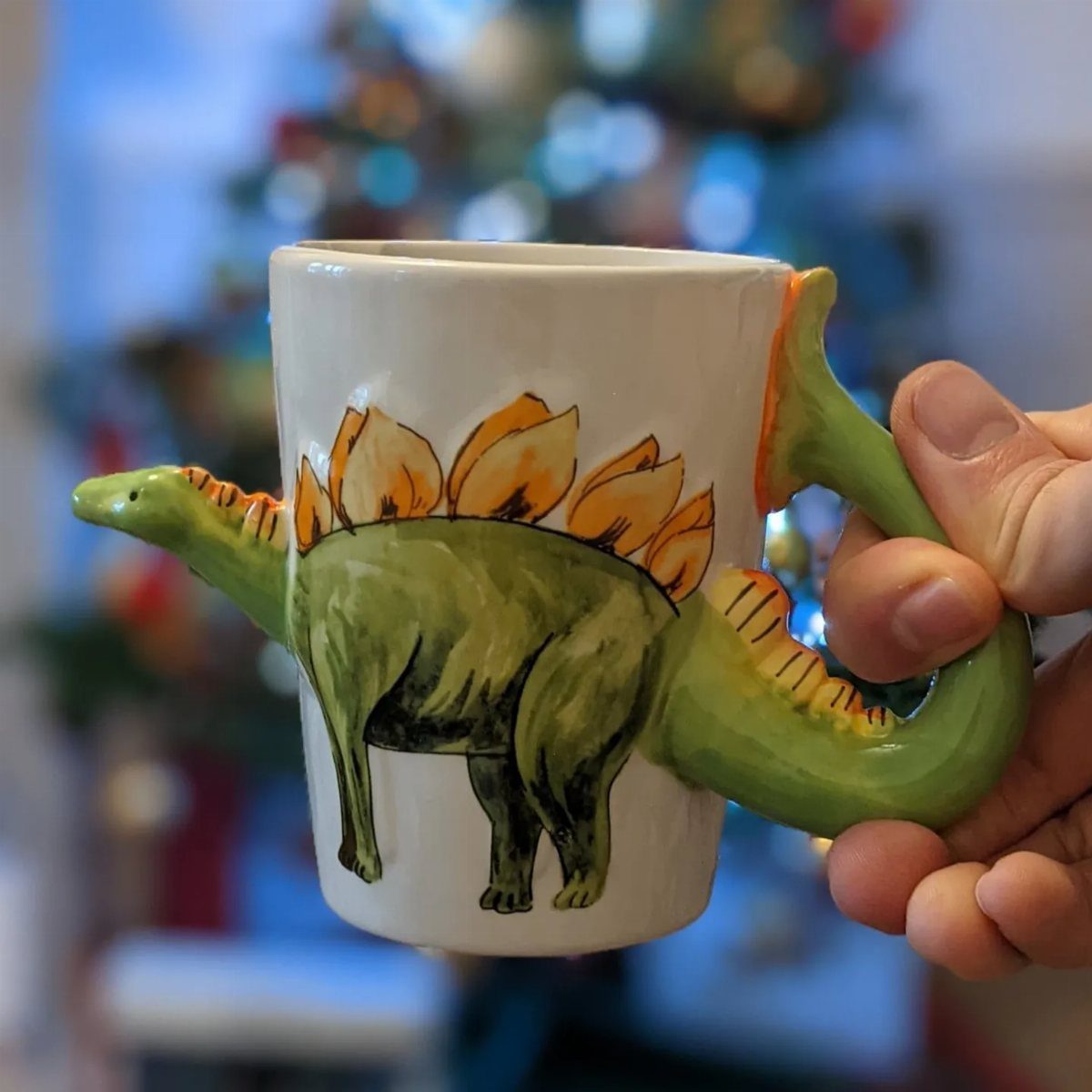 White ceramic mug with a 3D green stegosaurus design and orange plates.