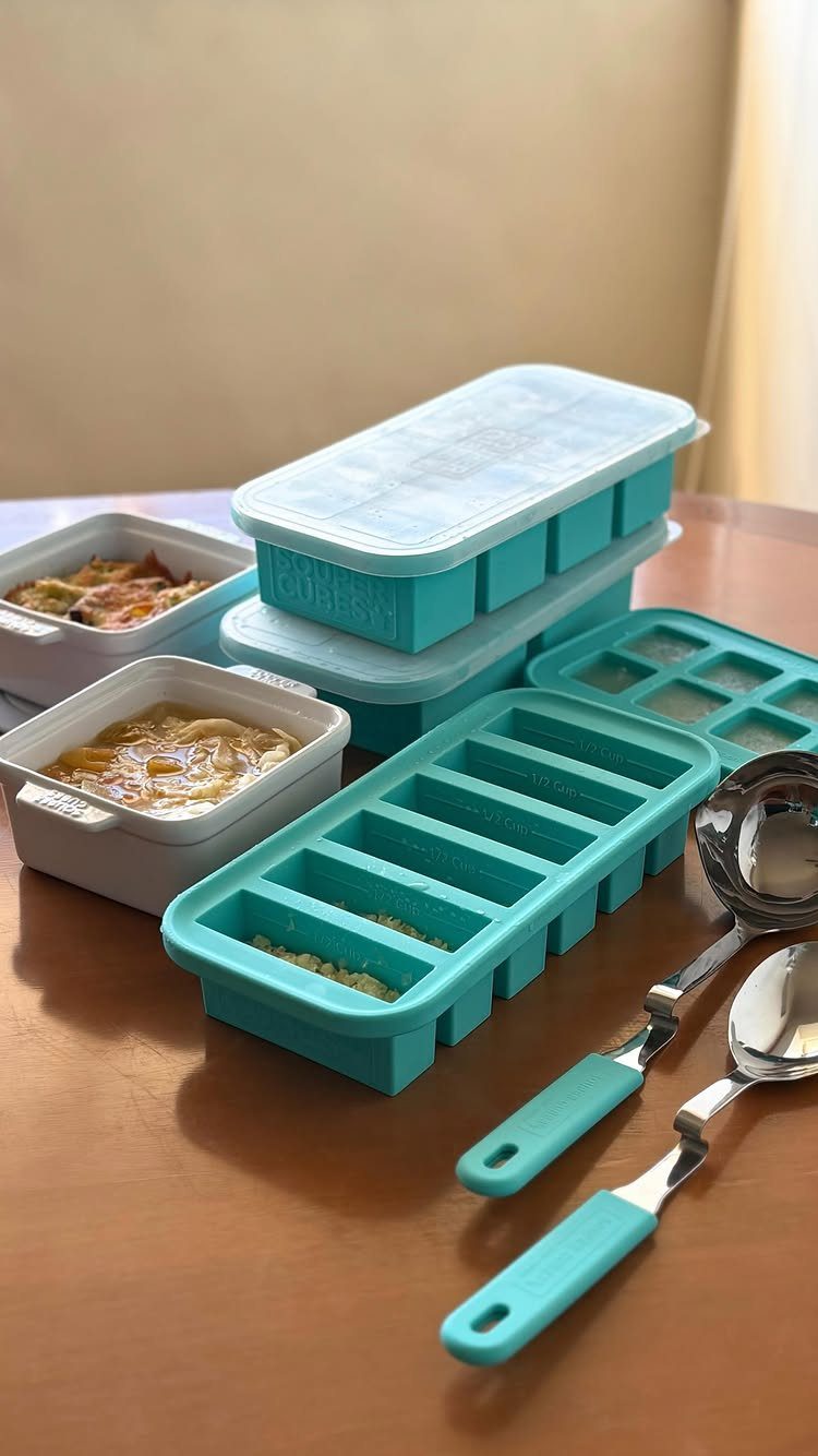 Teal silicone freezer molds with lids and matching spoons on a wooden table.