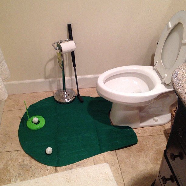 Mini golf putting mat and balls set up on a bathroom floor next to a toilet.